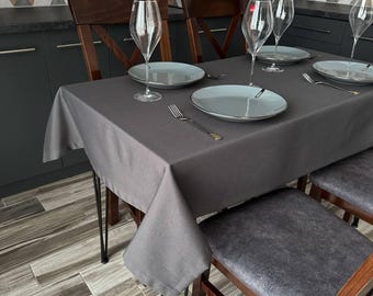 May include: A dark gray tablecloth with a geometric pattern on the wall behind it. The tablecloth is on a wooden table with four chairs. There are four wine glasses and four plates on the table.