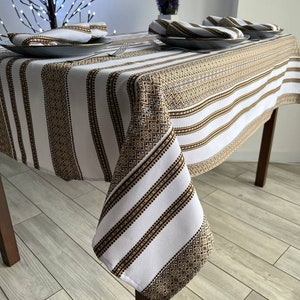 May include: White and gold striped tablecloth with a geometric pattern. The tablecloth is draped over a wooden table with a white background.