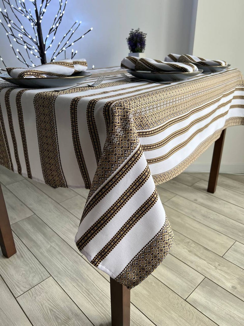 May include: White and gold striped tablecloth with a geometric pattern. The tablecloth is draped over a wooden table with a white background.