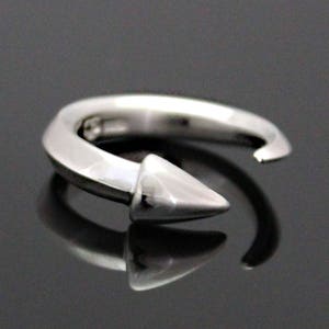 Può includere: Un anello d'argento con una punta appuntita. L'anello è aperto e ha una finitura liscia e lucida.