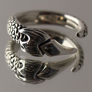 Puede incluir: Un anillo de plata con un dise&ntilde;o detallado de cola de pez. El anillo es abierto y ajustable.