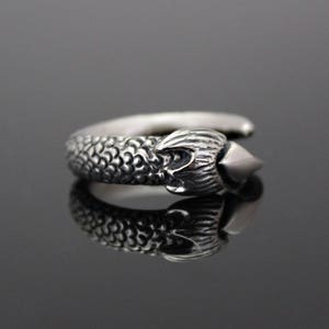 Puede incluir: Un anillo de plata con un dise&ntilde;o detallado de una cabeza de drag&oacute;n con una punta afilada en el extremo.