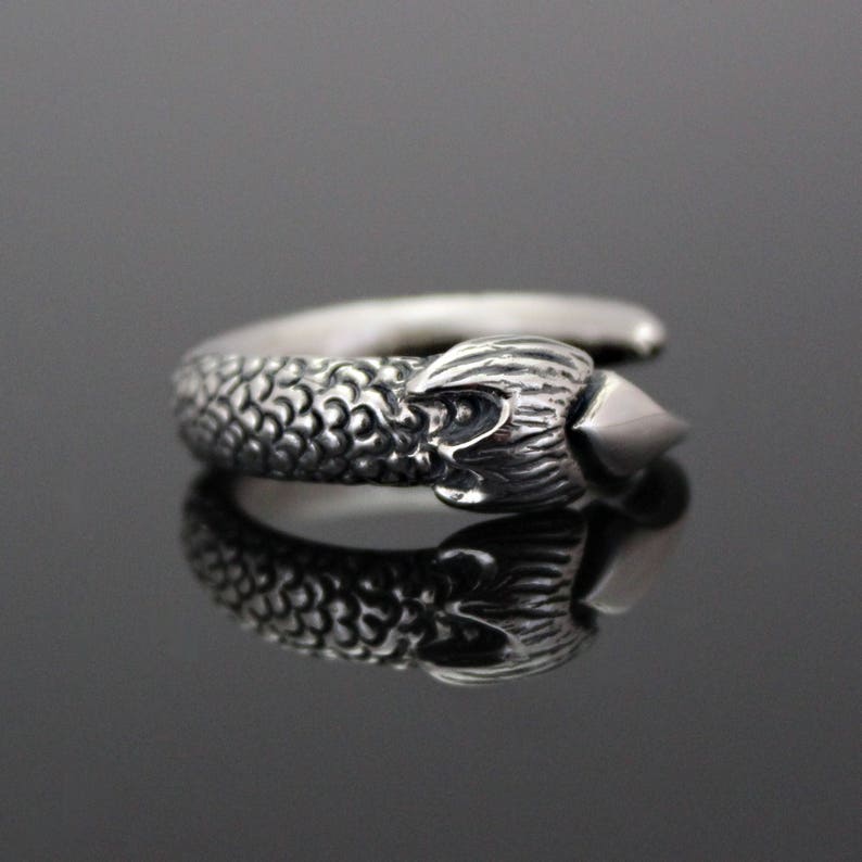 Puede incluir: Un anillo de plata con un dise&ntilde;o detallado de una cabeza de drag&oacute;n con una punta afilada en el extremo.