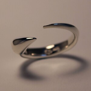 Puede incluir: Un anillo de plata con un dise&ntilde;o puntiagudo y curvo. El anillo est&aacute; abierto por un lado y tiene un acabado liso y pulido.