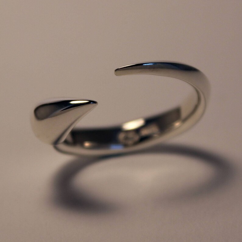 Puede incluir: Un anillo de plata con un dise&ntilde;o puntiagudo y curvo. El anillo est&aacute; abierto por un lado y tiene un acabado liso y pulido.