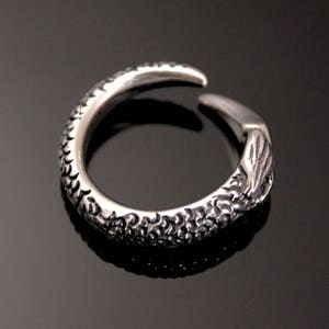 Puede incluir: Un anillo de plata con un dise&ntilde;o detallado que se asemeja a una garra o un tal&oacute;n. El anillo est&aacute; abierto y tiene una superficie texturizada.