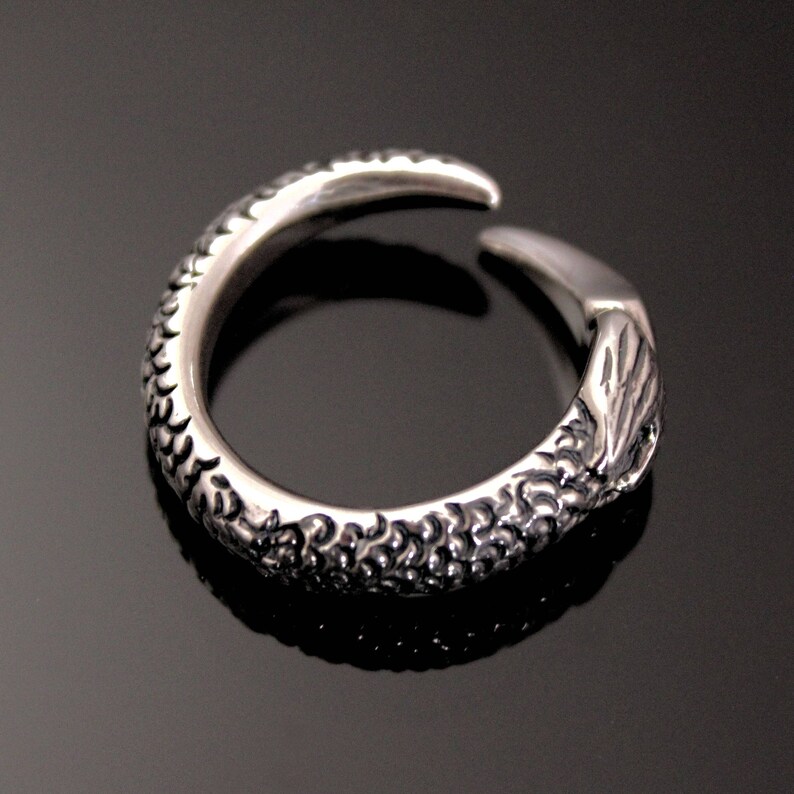 Puede incluir: Un anillo de plata con un dise&ntilde;o detallado que se asemeja a una garra o un tal&oacute;n. El anillo est&aacute; abierto y tiene una superficie texturizada.