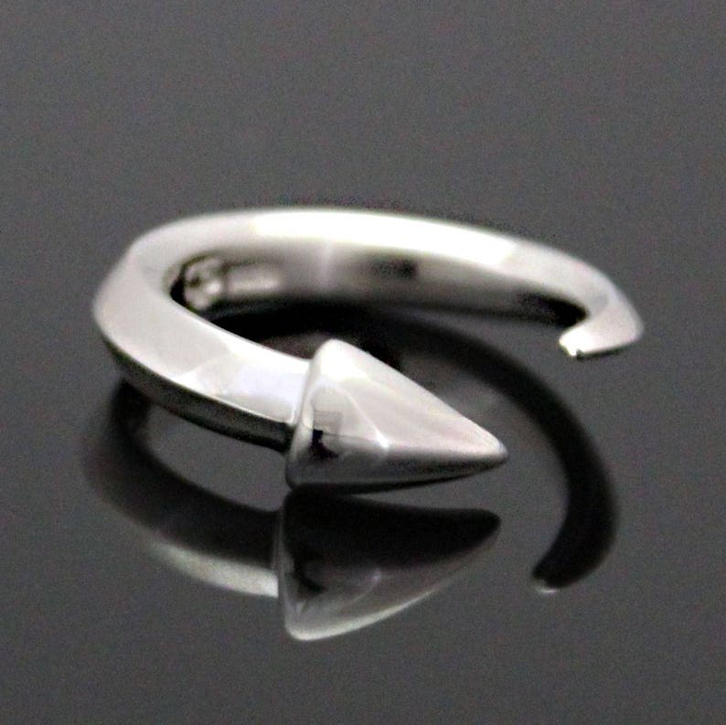 Puede incluir: Un anillo de plata con una punta puntiaguda. El anillo est&aacute; abierto y tiene un acabado liso y pulido.