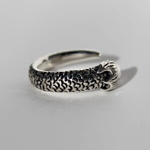 Puede incluir: Un anillo de plata con un dise&ntilde;o detallado de cabeza de serpiente en la banda.