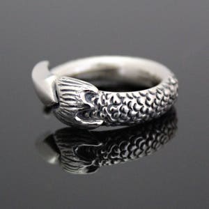 Puede incluir: Un anillo de plata con un dise&ntilde;o detallado de cola de sirena. La cola est&aacute; enroscada alrededor de la banda del anillo, y las escamas son visibles.