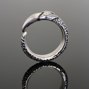 Puede incluir: Un anillo de plata con un dise&ntilde;o texturizado que se asemeja a una serpiente. El anillo tiene una cabeza detallada con un hocico puntiagudo y afilado.