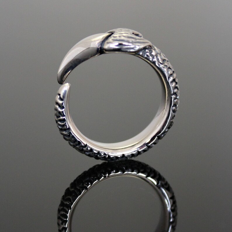 Puede incluir: Un anillo de plata con un dise&ntilde;o texturizado que se asemeja a una serpiente. El anillo tiene una cabeza detallada con un hocico puntiagudo y afilado.