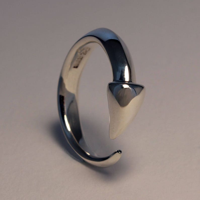 Puede incluir: Un anillo de plata con un dise&ntilde;o puntiagudo en forma de flecha. El anillo est&aacute; abierto y tiene un acabado liso y pulido.