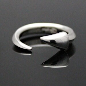 Puede incluir: Un anillo de plata con un dise&ntilde;o puntiagudo y curvo. El anillo est&aacute; abierto y tiene un acabado liso y pulido.