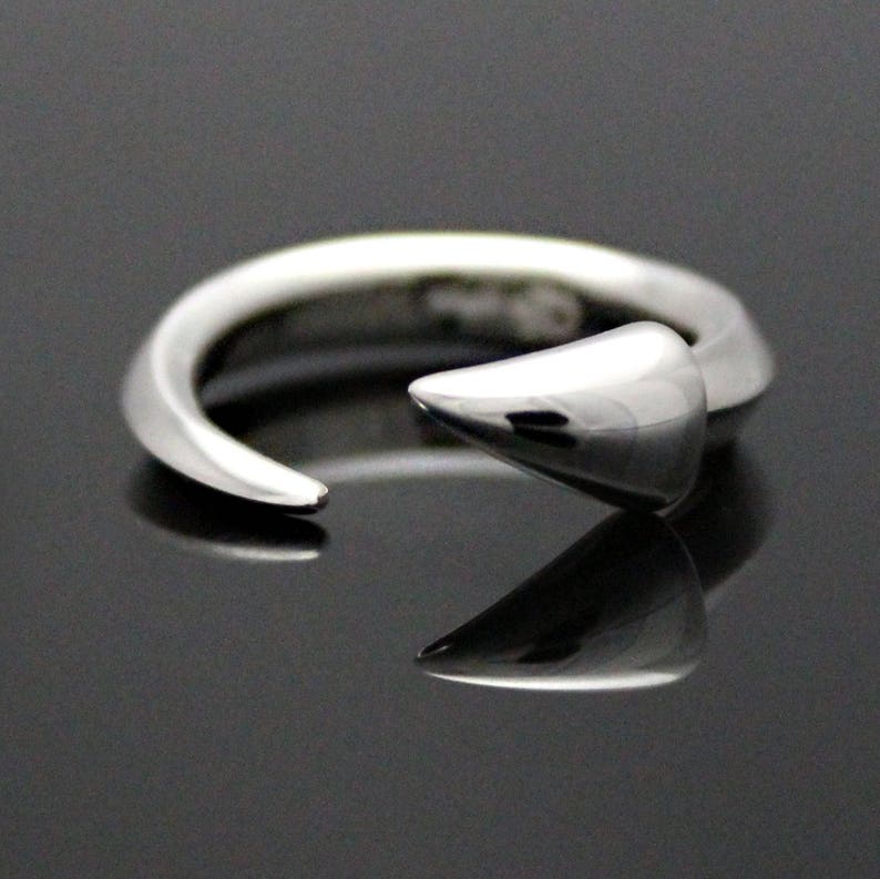 Puede incluir: Un anillo de plata con un dise&ntilde;o puntiagudo y curvo. El anillo est&aacute; abierto y tiene un acabado liso y pulido.
