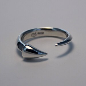 Puede incluir: Un anillo de plata con un dise&ntilde;o puntiagudo y curvo. El anillo est&aacute; abierto por un lado y tiene un acabado liso y pulido.