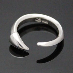 Puede incluir: Un anillo de plata con un dise&ntilde;o puntiagudo y curvo. El anillo est&aacute; abierto y tiene un acabado liso y pulido.
