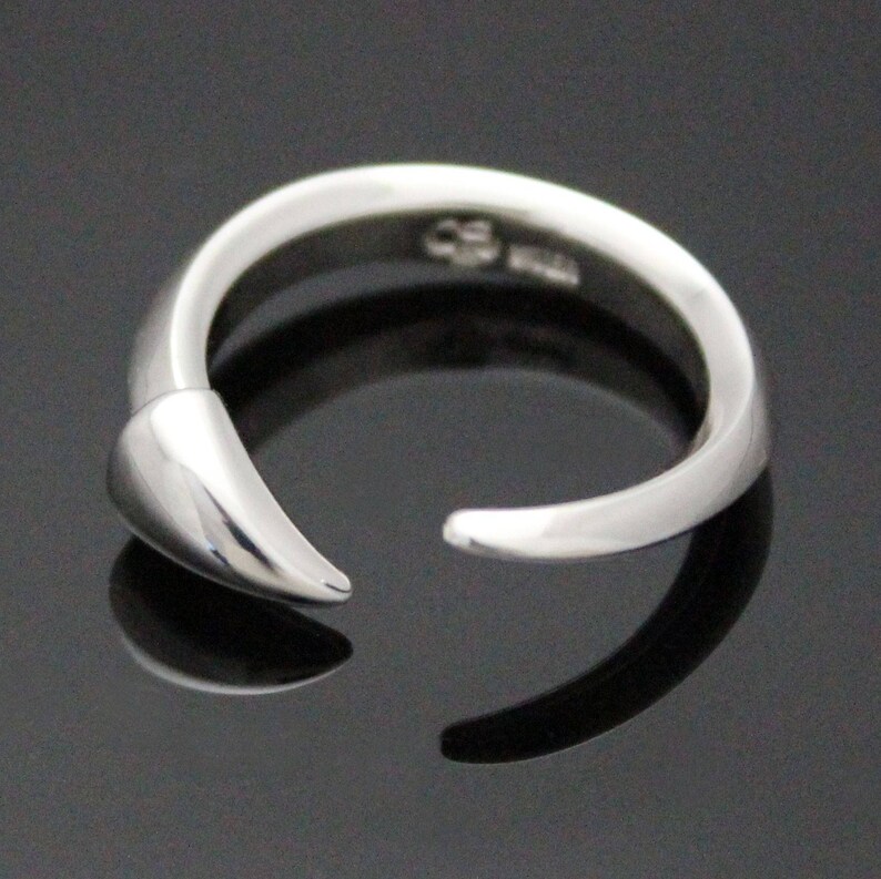 Puede incluir: Un anillo de plata con un dise&ntilde;o puntiagudo y curvo. El anillo est&aacute; abierto y tiene un acabado liso y pulido.