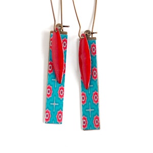 May include: A pair of turquoise and red dangle earrings with a geometric pattern. The earrings have a red teardrop-shaped charm hanging from the bottom.