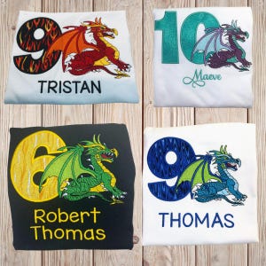 May include: Four children's birthday shirts with dragon designs. The shirts are white and black, with embroidered numbers and dragon illustrations in various colors. Each shirt has a name embroidered below the number and dragon.