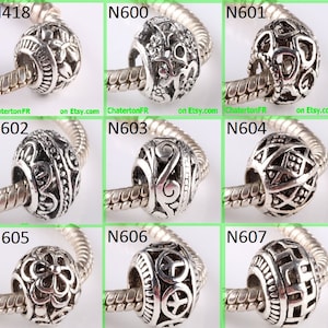 May include: Nine silver charm beads with intricate designs, including floral, geometric, and scroll patterns. The beads are displayed on a silver chain.