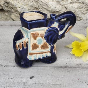 Peut inclure: Un pot de fleurs en céramique bleu et blanc en forme d'éléphant avec des motifs géométriques marrons et blancs. Le pot a une petite ouverture en haut pour planter.