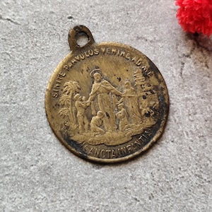Könnte beinhalten: Vintage religiöse Medaille aus Bronze mit Aufhängeschlaufe. Die Medaille zeigt eine geprägte Szene mit einer Figur und Kindern, umgeben von Text. Die Ränder weisen Abnutzungserscheinungen auf.