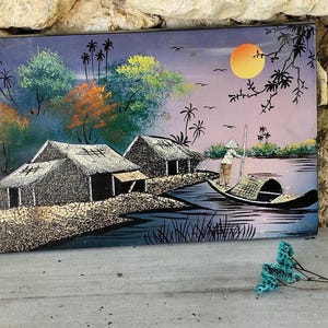 Peut inclure: Tableau rectangulaire représentant un paysage fluvial serein avec des huttes et un bateau. L'œuvre présente un coucher de soleil avec un soleil jaune, des palmiers et une personne dans un bateau. La palette de couleurs comprend des bleus, des verts et des oranges.