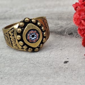 Può includere: Un anello d'oro con un design decorativo e un occhio in mosaico colorato al centro.