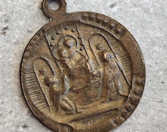 May include: A circular bronze-toned metal pendant featuring a raised relief design of a central figure seated on a throne flanked by two kneeling figures under arched structures. The pendant has a small circular loop at the top for suspension.