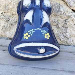 Könnte beinhalten: Eine blaue, glockenförmige Keramikform mit weißen und gelben floralen Akzenten. Die Form hat oben ein Loch zum Aufhängen.