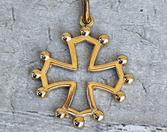 May include: A gold-colored pendant in the shape of a cross. The cross has a stylized design with rounded edges and small spheres at the ends of each arm. The pendant has a loop at the top for a chain.