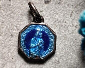 Puede incluir: Un colgante octogonal de plata con una imagen de esmalte azul de un santo. El colgante tiene un bucle en la parte superior para sujetarlo a una cadena.