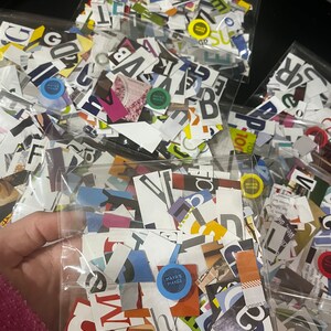 May include: A clear plastic bag filled with colorful paper scraps, including letters, numbers, and other shapes. The bag is labeled "MAYA'S MAKES".