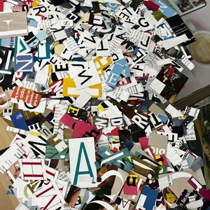 May include: A large pile of colorful, cut-out letters from magazines. The letters are in various fonts and sizes, and some are overlapping. The letters are mostly black, white, and red, but there are also some blue, green, and yellow letters.