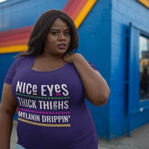 May include: Purple t-shirt with the text "Nice Eyes Thick Thighs Melanin Drippin'" in a colorful, geometric font.