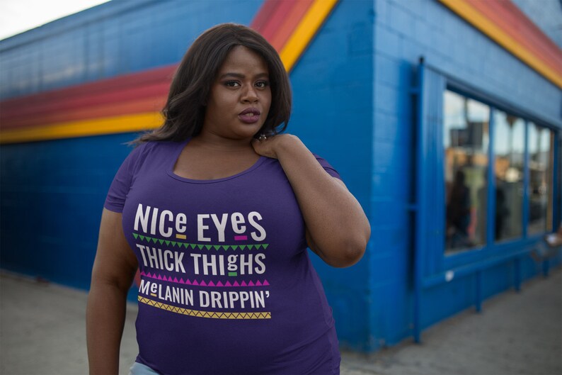 May include: Purple t-shirt with the text "Nice Eyes Thick Thighs Melanin Drippin'" in a colorful, geometric font.