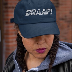 May include: A navy blue baseball cap with a white embroidered design of motorcycles and the word "BRAAP!"