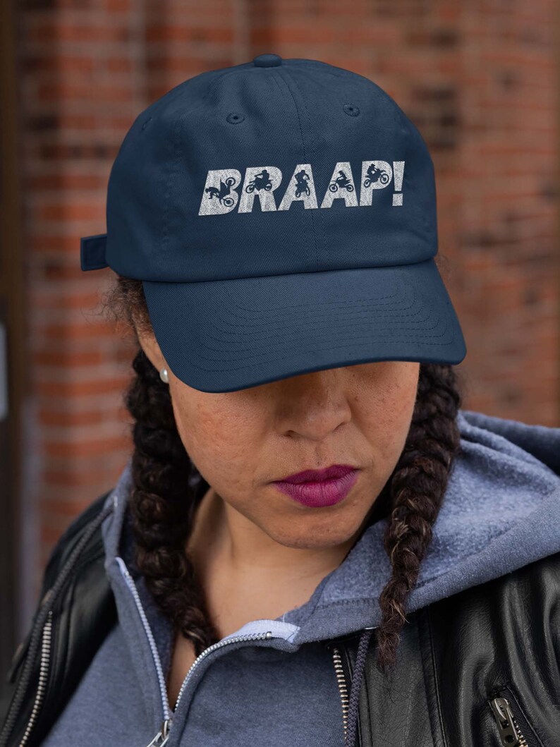 May include: A navy blue baseball cap with a white embroidered design of motorcycles and the word "BRAAP!"