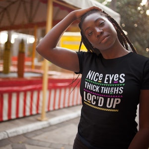 May include: Black t-shirt with the text "Nice Eyes Thick Thighs Loc'd Up" in colorful letters.