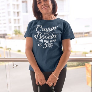 K&ouml;nnte beinhalten: Eine Frau tr&auml;gt ein marineblaues T-Shirt mit dem Text "Cruisin' and Boozin' all the way to 5-0" in Wei&szlig;. Das Shirt zeigt ein nautisches Rad-Motiv.