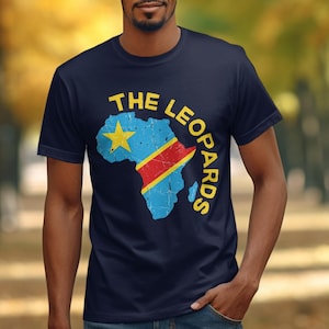 May include: A navy blue short-sleeve t-shirt featuring a distressed graphic of the African continent filled with the flag of the Democratic Republic of the Congo, including a yellow star and red diagonal stripe, with the text THE LEOPARDS in yellow.