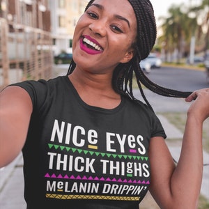 May include: Black t-shirt with a white graphic that says "NICE EYES THICK THIGHS MELANIN DRIPPIN'" in a colorful, patterned font.