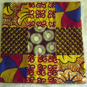 May include: A patchwork fabric with nine squares, each with a different colorful pattern. The patterns include swirls, flowers, and geometric shapes. The fabric is primarily yellow, red, blue, and brown.