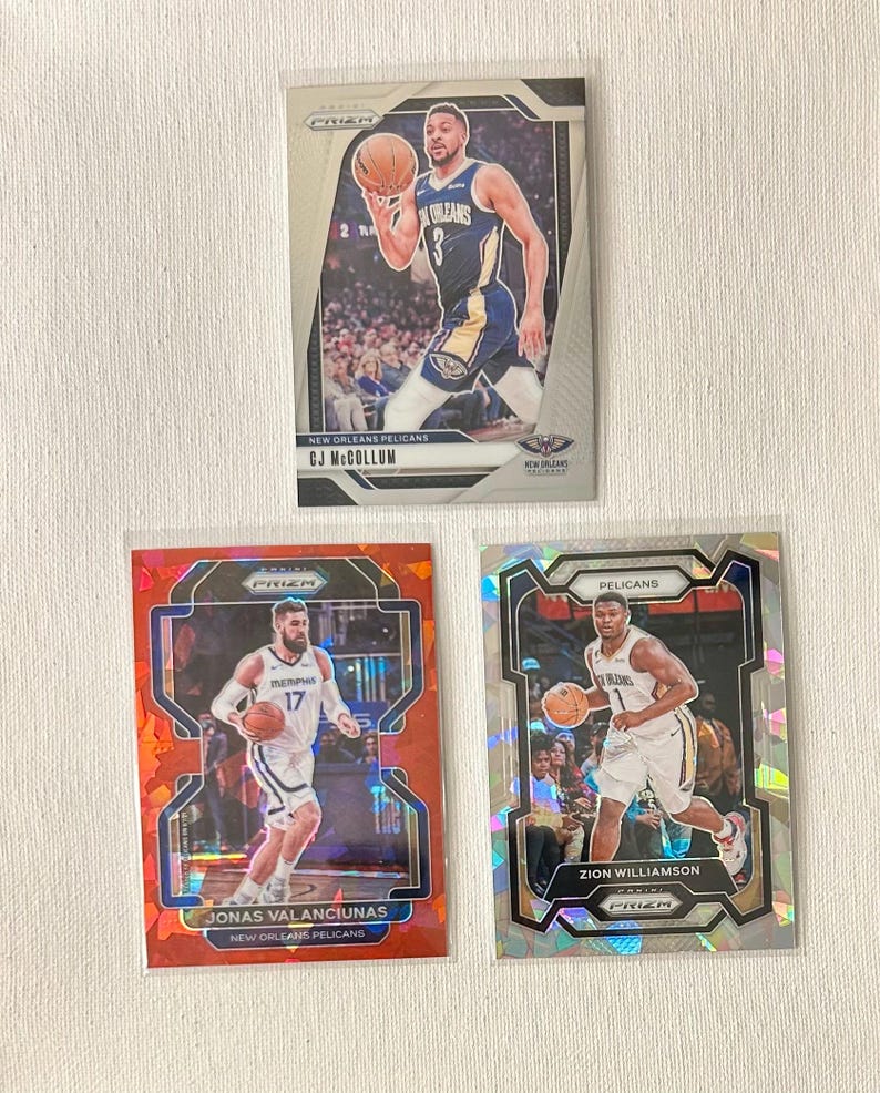 May include: Three basketball trading cards featuring New Orleans Pelicans players. The cards display CJ McCollum, Jonas Valanciunas, and Zion Williamson. Each card has a player image, team logo, and player name. The cards are in protective sleeves.
