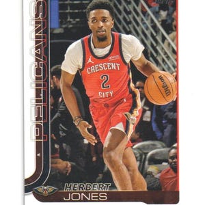 May include: A Topps trading card featuring Herbert Jones of the New Orleans Pelicans. Jones is wearing a red and white basketball jersey with the number 2. He is dribbling an orange Wilson basketball. The card has the Pelicans logo and team name.