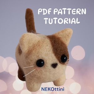 Può includere: Figurina di gatto in feltro fatta a mano, beige e marrone, con grandi occhi neri e baffi bianchi. Il testo "PDF PATTERN TUTORIAL" è sopra il gatto e "NEKOttini" sotto. Il gatto ha una piccola coda dritta.