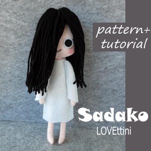 Può includere: Bambola in feltro fatta a mano di Sadako, un personaggio con lunghi capelli neri e un vestito bianco. La bambola ha un viso semplice con un occhio grande. Il testo "pattern + tutorial" e "Sadako LOVettini" è incluso.