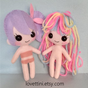 Puede incluir: Dos mu&ntilde;ecas de fieltro hechas a mano con pelo de lana. Una mu&ntilde;eca tiene el pelo morado y un traje de ba&ntilde;o rosa. La otra mu&ntilde;eca tiene el pelo de lana arco&iacute;ris y est&aacute; desnuda. Las mu&ntilde;ecas est&aacute;n de pie sobre una superficie azul claro. El texto "lovettini.etsy.com" est&aacute; en la parte inferior de la imagen.