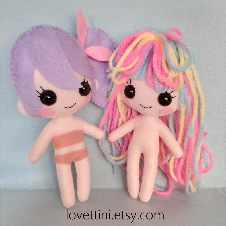 Puede incluir: Dos mu&ntilde;ecas de fieltro hechas a mano con pelo de lana. Una mu&ntilde;eca tiene el pelo morado y un traje de ba&ntilde;o rosa. La otra mu&ntilde;eca tiene el pelo de lana arco&iacute;ris y est&aacute; desnuda. Las mu&ntilde;ecas est&aacute;n de pie sobre una superficie azul claro. El texto "lovettini.etsy.com" est&aacute; en la parte inferior de la imagen.